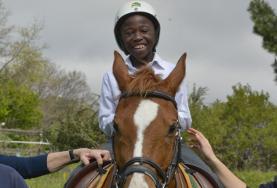 Volunteer Care A volunteer supports a disabled boy as he rides his therapy horse at our Equine Therapy placement in South Africa.